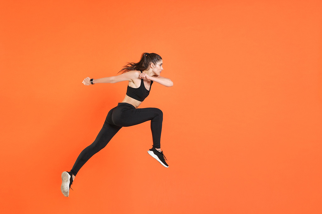 Une femme pose comme si elle courait contre un fond orange vif.