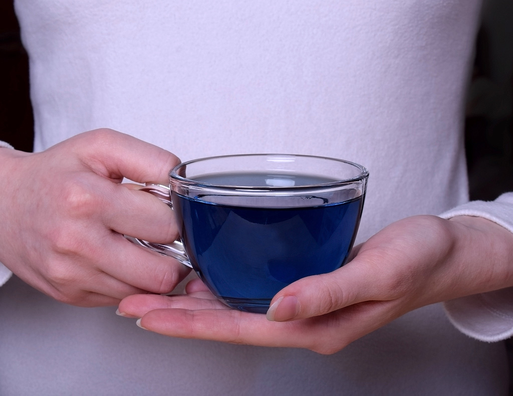 Une femme tenant une tasse de thé bleu devant son ventre.